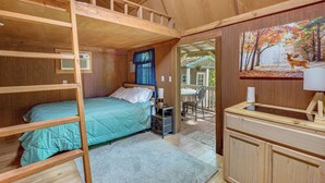 L’intérieur d’un chalet en bois comprend des lits superposés, un coin cuisine et un tableau représentant une scène de forêt.