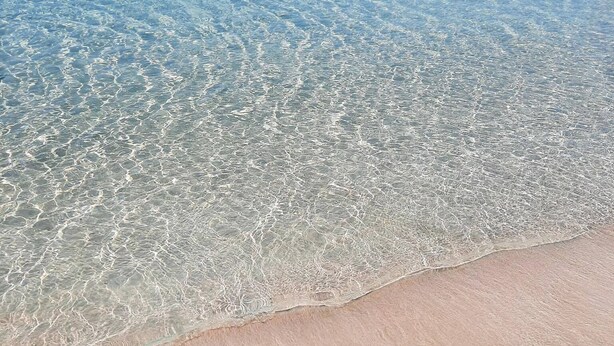 Una spiaggia con acque poco profonde e cristalline e una riva sabbiosa.