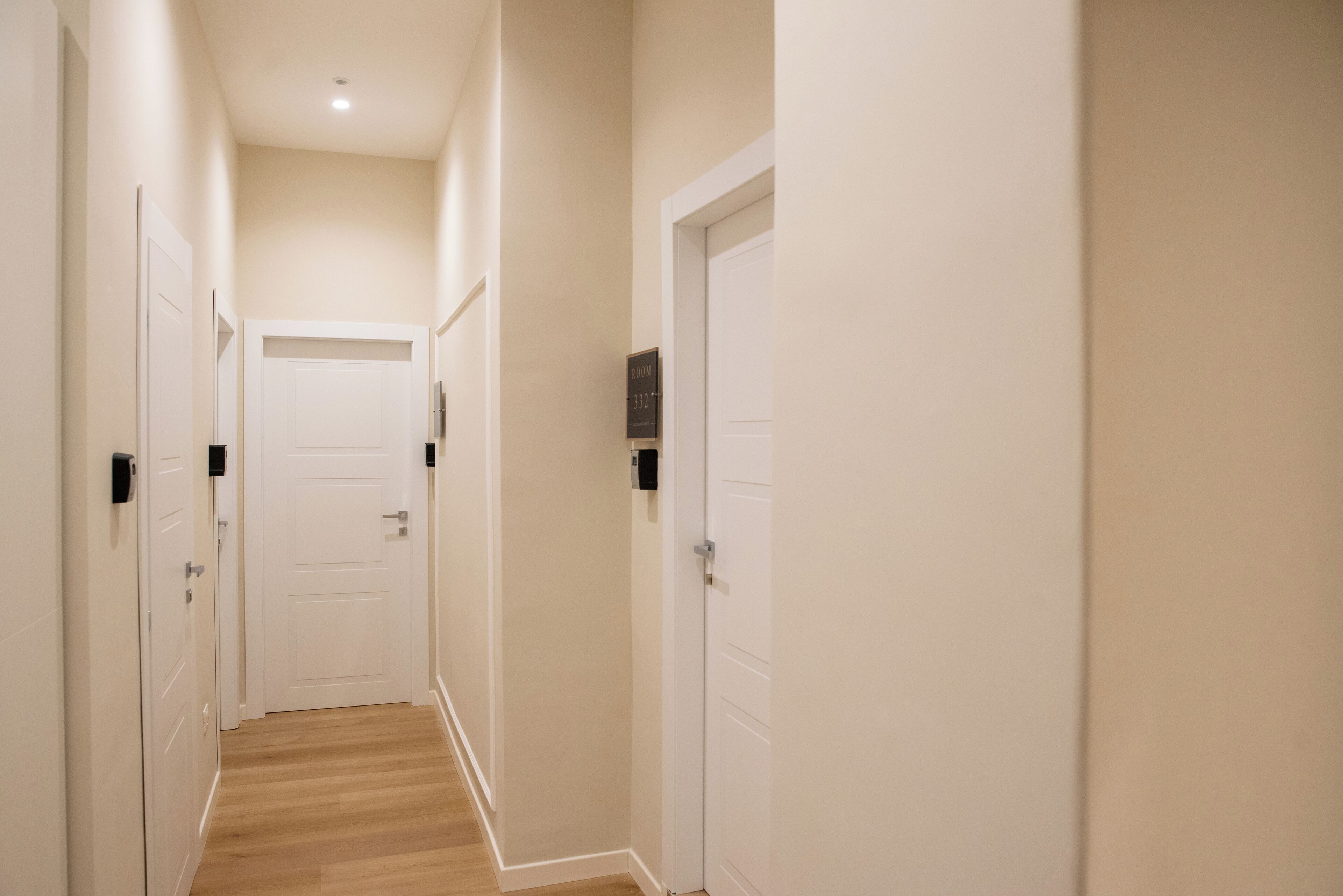 A narrow hallway with white doors, wooden flooring, and a ceiling light.