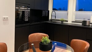 A modern kitchen with black cabinets, a glass dining table, and brown leather chairs. - Apartment mit Parkblick, Stilvolle Einrichtung, 1,1km vom Hauptbahnhof Entfernt (Bremerhaven)
