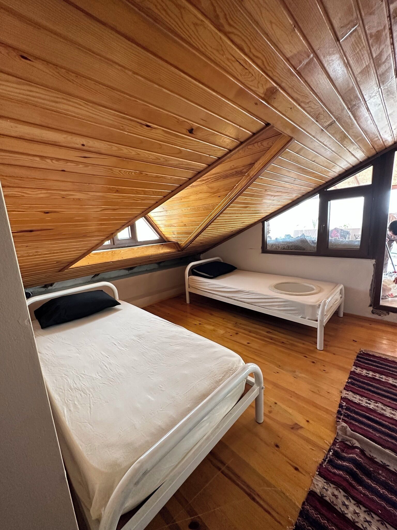 Un dormitorio acogedor en el ático, con techos de listones de madera, dos camas individuales y un ventanal que ofrece vistas al exterior.