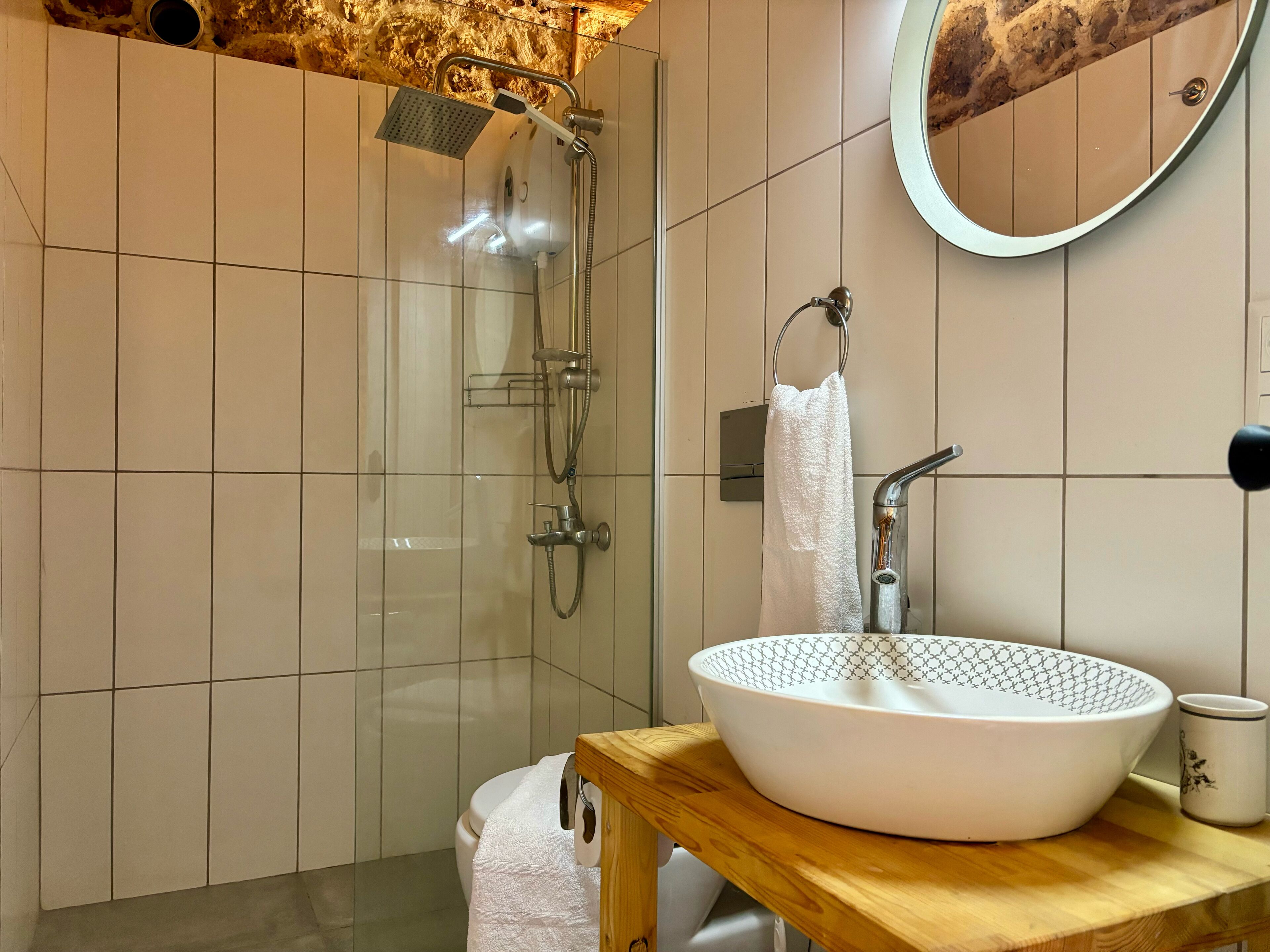 A modern bathroom with a glass-enclosed shower, a wooden vanity with a white sink, and a round mirror.