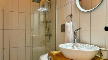 A modern bathroom with a glass-enclosed shower, a wooden vanity with a white sink, and a round mirror.