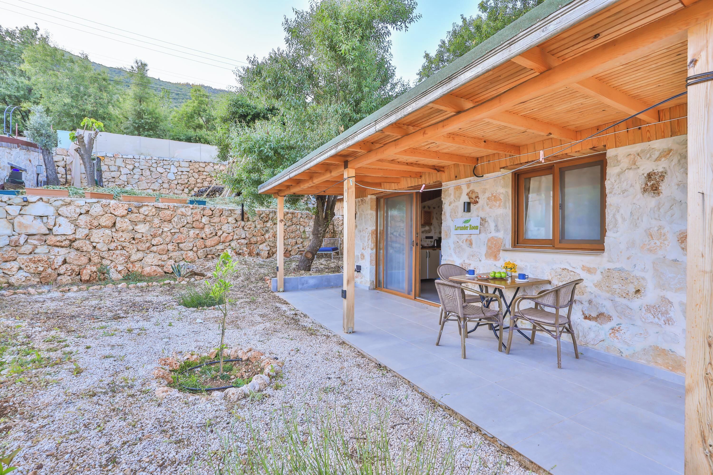 Un bâtiment rustique en pierre, doté d’un porche en bois et d’une table entourée de chaises.