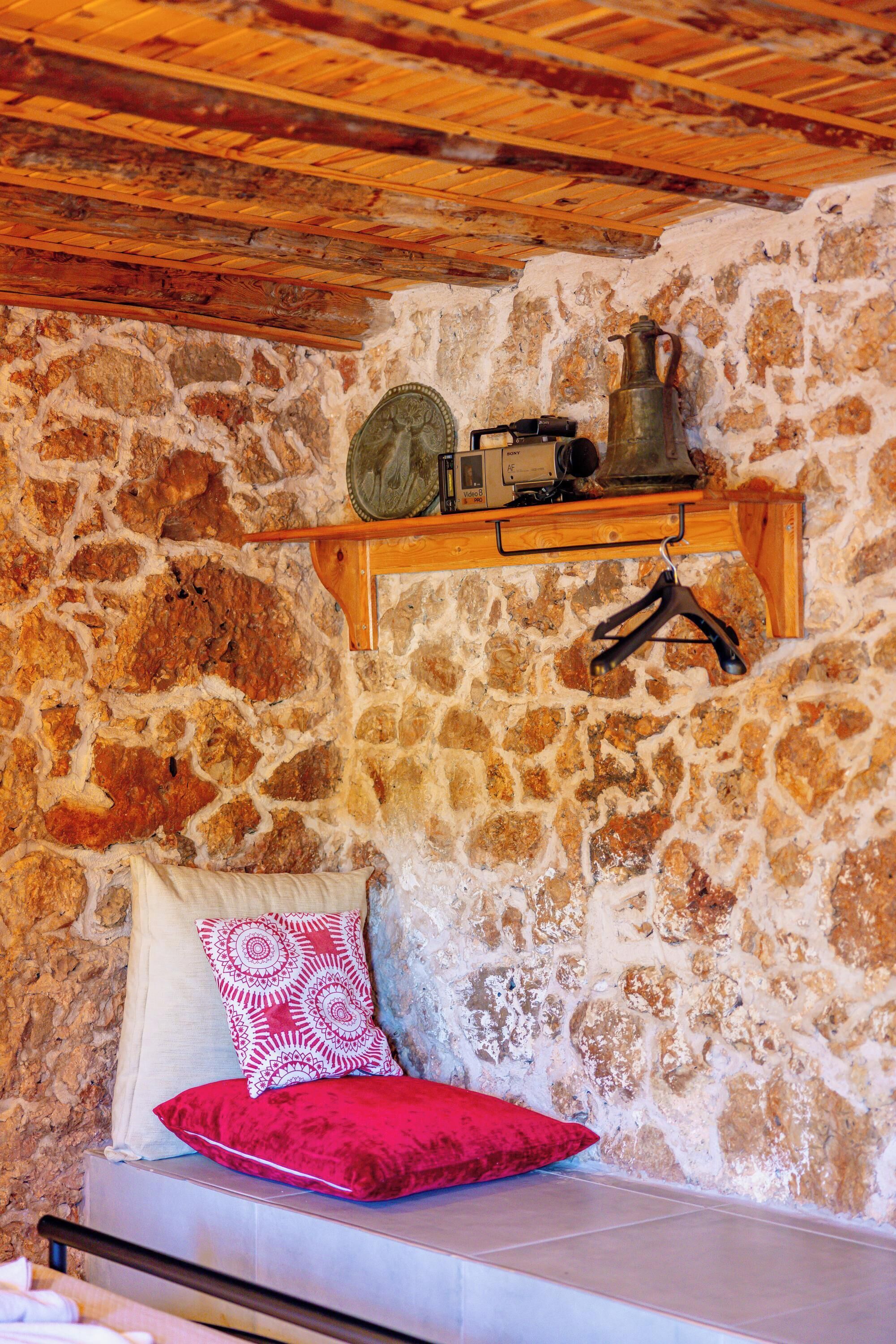 Un muro in pietra con uno scaffale di legno che contiene una macchina fotografica vintage, un contenitore metallico e un appendiabiti nero.