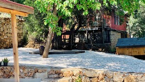 Un patio de piedra con una pérgola de madera, un pequeño jardín con plantas en macetas y una rústica pared de piedra.