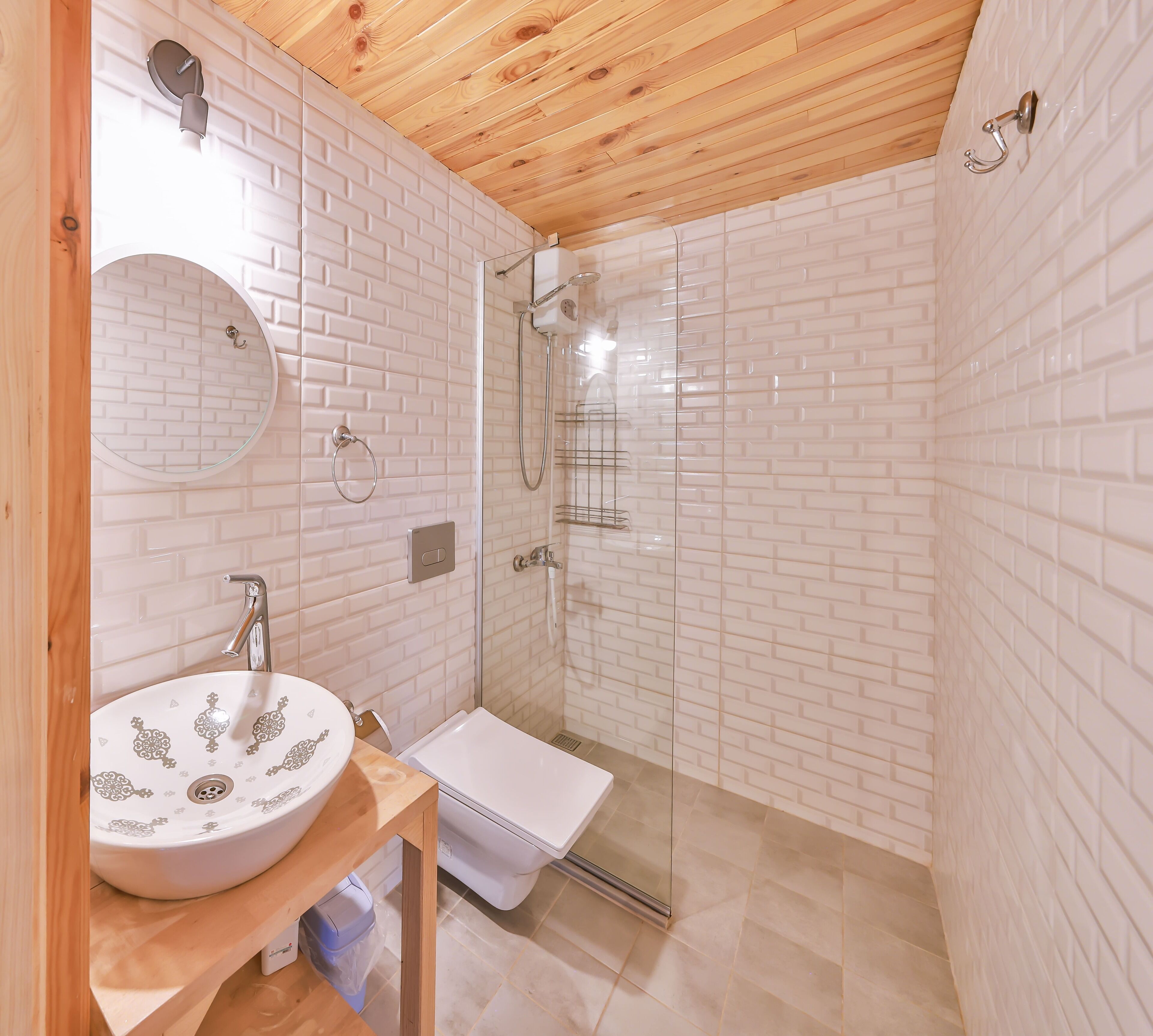 Un baño con lavamanos blanco, espejo y cabina de ducha con mampara de vidrio.