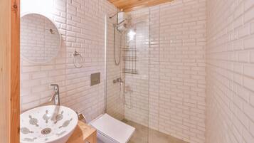Un baño con lavamanos blanco, espejo y cabina de ducha con mampara de vidrio.