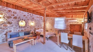 Una habitación rústica con pared de piedra, techo de madera, un sofá, una mesa de comedor con sillas y una cama.