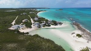 An aerial view of a coastal property with multiple buildings, a sandy beach, and turquoise waters.