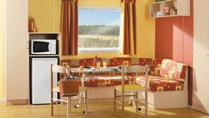 A compact room with a kitchenette, a sofa, a dining table with chairs, and a window with curtains.