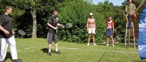 Un grupo de personas jugando tenis en un campo cubierto de césped, con árboles al fondo.