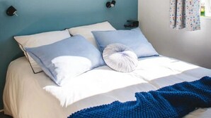 A neatly made bed with a blue blanket, two pillows, and a wall-mounted shelf above it.