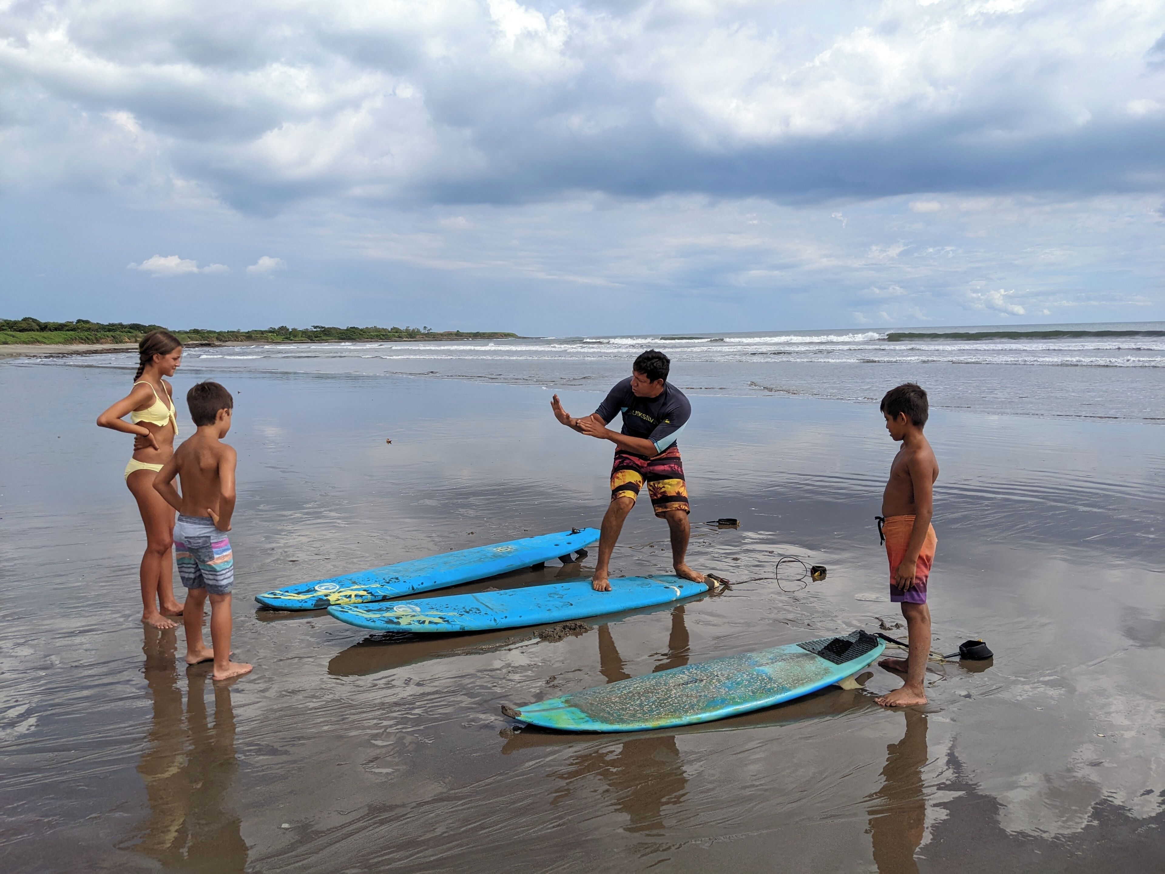 A beach scene with people standing near surfboards.