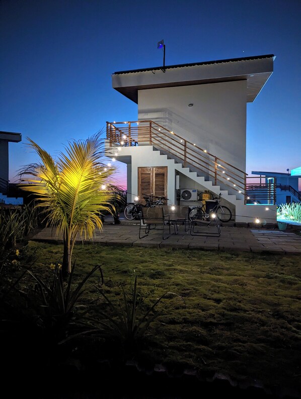 A modern building with a staircase leading to a balcony, surrounded by greenery and outdoor seating.
