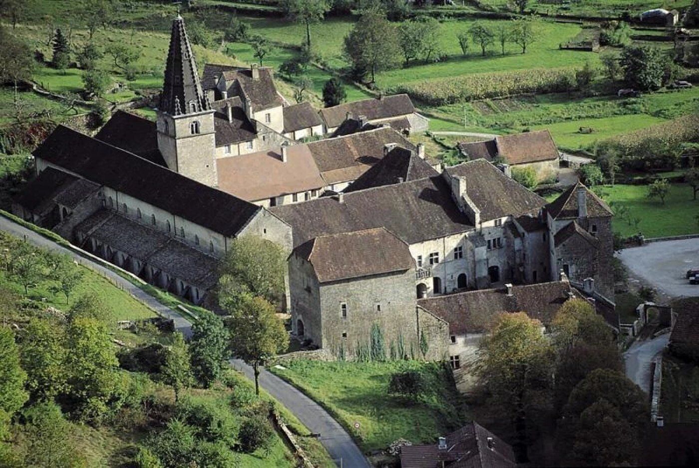 A large, historic building with multiple wings and a prominent tower, surrounded by lush green fields.