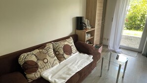 A living room with a brown sofa, a white throw blanket, a glass coffee table, and a wooden cabinet with kitchen items.