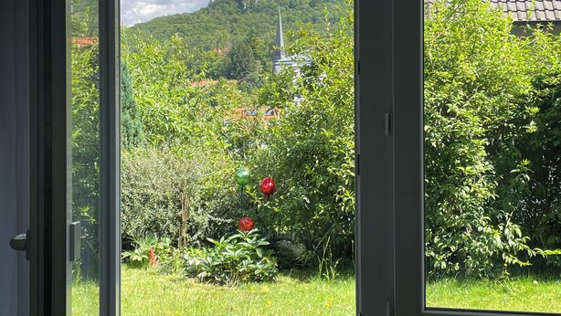 A view through a door of a lush garden with a hill in the background.