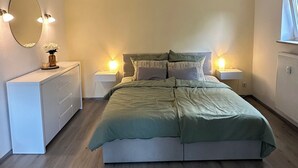A bedroom with a bed, bedside tables, a dresser, a mirror, and a ceiling light fixture.