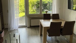 A modern dining area with a table and chairs, large windows with curtains, a ceiling light, and a TV mounted on the wall.