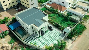 A residential building with a swimming pool, multiple cars parked, and lush greenery. - Exclusive Villa in Hideout East Legon (Accra)