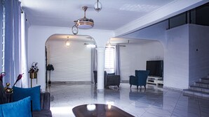 A spacious living area with a marble floor, a dark wooden coffee table, a grey sofa with blue cushions, a blue armchair, and a flat-screen TV. - Exclusive Villa in Hideout East Legon (Accra)