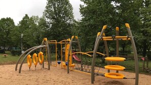 Un parque infantil con juegos amarillos y grises, incluyendo columpios y estructuras para escalar, sobre una superficie de arena.