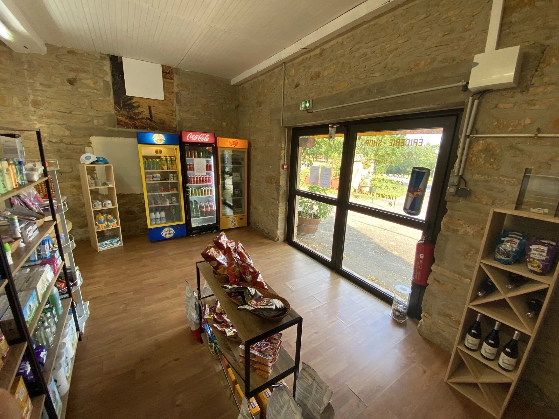 Un magasin dont les étagères sont remplies d’en-cas et de boissons, avec un réfrigérateur Coca-Cola et une étagère à vin.