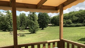 Una terraza de madera con una mesa y sillas, con vistas a un área verde con árboles y un edificio a lo lejos.
