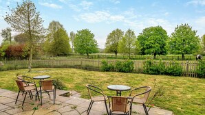A patio area with stone flooring and wicker chairs, surrounded by a wooden fence and lush greenery. - 4 bedroom accommodation in Hilmarton, near Calne (Hilmarton, near Calne)