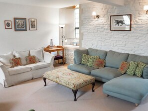 A living room with a white stone wall, a blue sofa, a white sofa, and a floral ottoman. There are framed pictures on the wall and a lamp on a side table. - 4 bedroom accommodation in Hilmarton, near Calne (Hilmarton, near Calne)