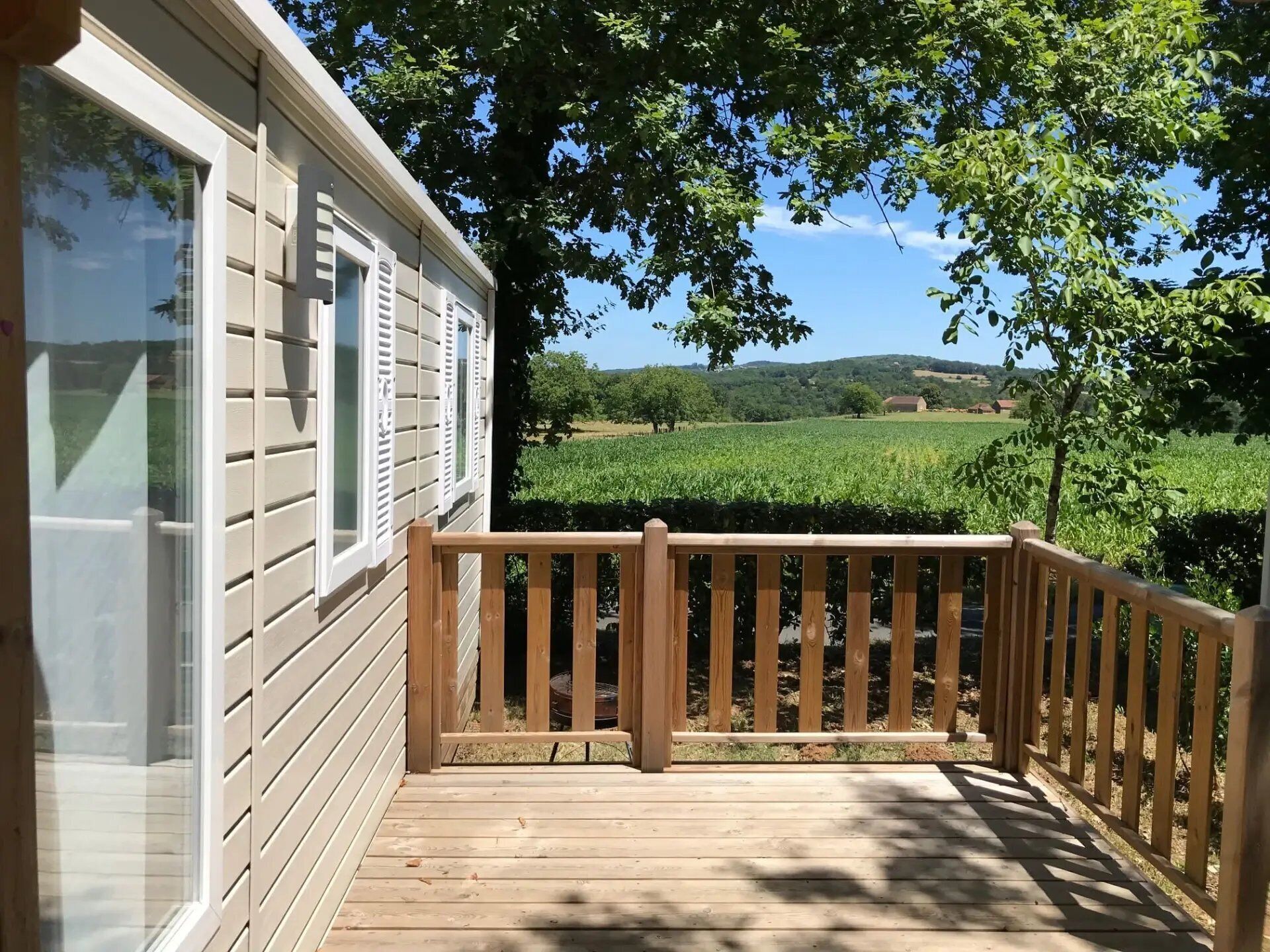 A wooden deck with a railing, a house with white siding and shutters, and a vineyard in the background.