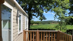 A wooden deck with a railing, a house with white siding and shutters, and a vineyard in the background.