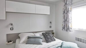 A modern bedroom with a bed, pillows, a bedside table, and a window with curtains.
