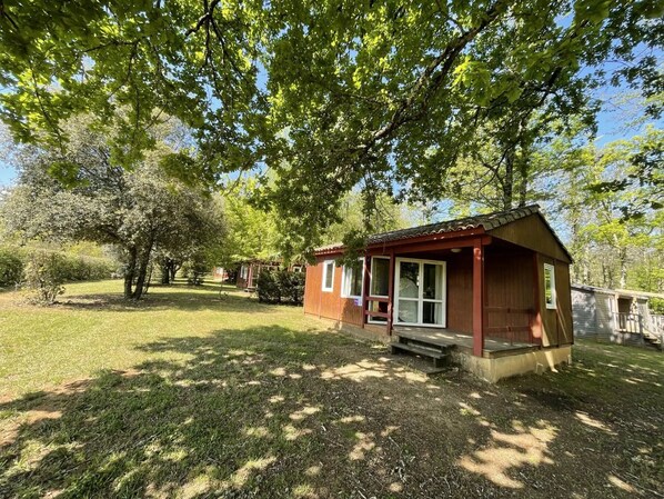 A small wooden cabin with a porch, surrounded by trees and grass. - ZEcamping 4* piscine chauffée dog friendly animations chalet 28m2 (Proissans)