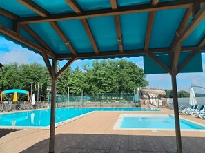 Un espace piscine couvert, doté de chaises longues et offrant une vue sur les arbres.