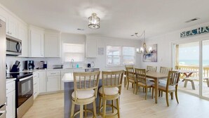 A modern kitchen with white cabinets, a central island with chairs, and a view of the sea through large windows.