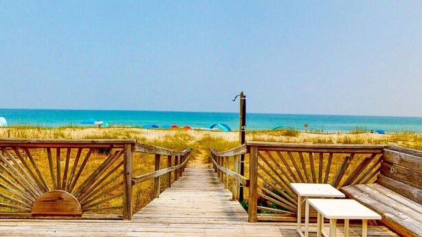 A wooden boardwalk leading to a beach with a bench and a signpost.