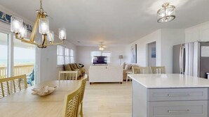 A modern kitchen with a central island, a dining area with wooden chairs, and a view of the ocean.
