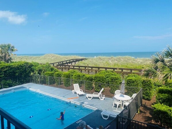Une piscine avec des chaises longues et une terrasse en bois donnant sur la plage.