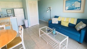 Uma sala de estar com um sofá azul, uma mesa de centro e uma área de jantar com uma mesa e cadeiras de madeira.