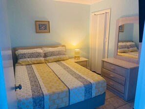 A bedroom with a bed, bedside table with a lamp, a dresser, and a door.