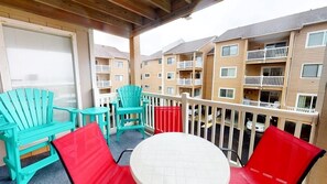 A balcony with turquoise chairs, a red chair, and a white table.