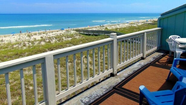 A balcony with a view of the beach and ocean, featuring a wooden deck and white outdoor furniture. - Sands 4 3-A-2 bedroom 2 bath, 3rd floor condo with sweeping views from the Master and living room (Carolina Beach)