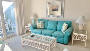 A living room with a teal sofa, two side tables with lamps, a glass coffee table, and a framed picture on the wall. - Sands 4 3-A-2 bedroom 2 bath, 3rd floor condo with sweeping views from the Master and living room (Carolina Beach)