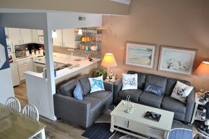 A living room with a grey sofa set, a coffee table, and a kitchen area in the background.