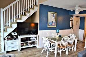 Un salon avec un téléviseur, des meubles blancs, un escalier et un tableau accroché au mur.