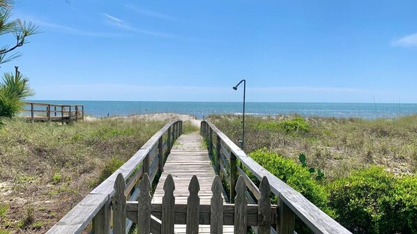 A wooden boardwalk leading to a beach with a clear view of the ocean.
