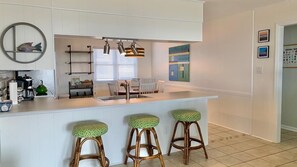 Una cocina moderna con una isla central, tres taburetes y una lámpara colgante.