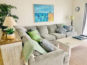 En stue med en grå sofa, et sofabord, en lampe, et billede og et ur på væggen.
